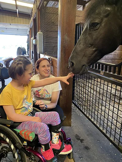 Child in wheelchair touching horses nose